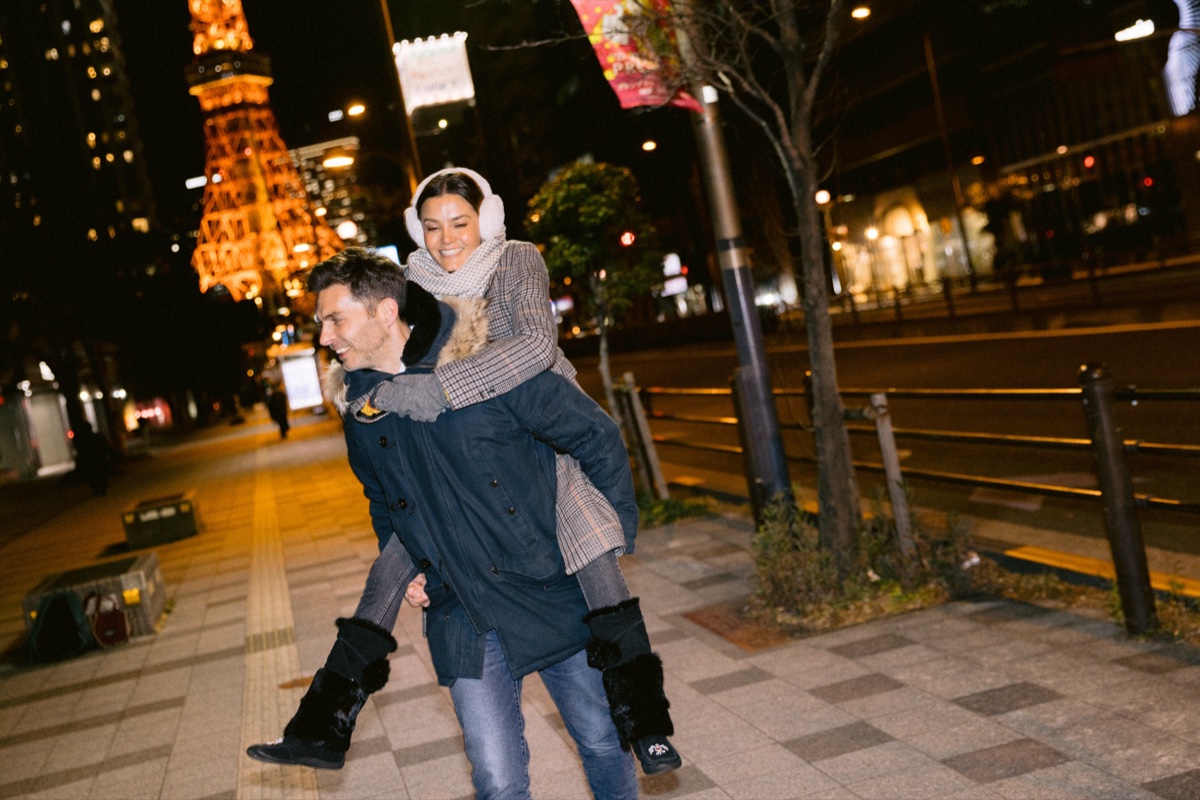 Couple laughing on a piggyback ride with Tokyo Tower lit up behind them
